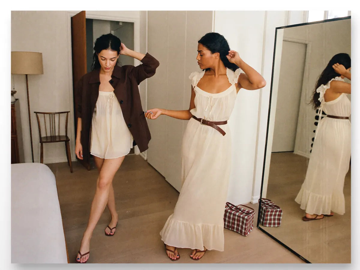 Two women styling an ivory maxi dress with a brown blazer beside a mirror