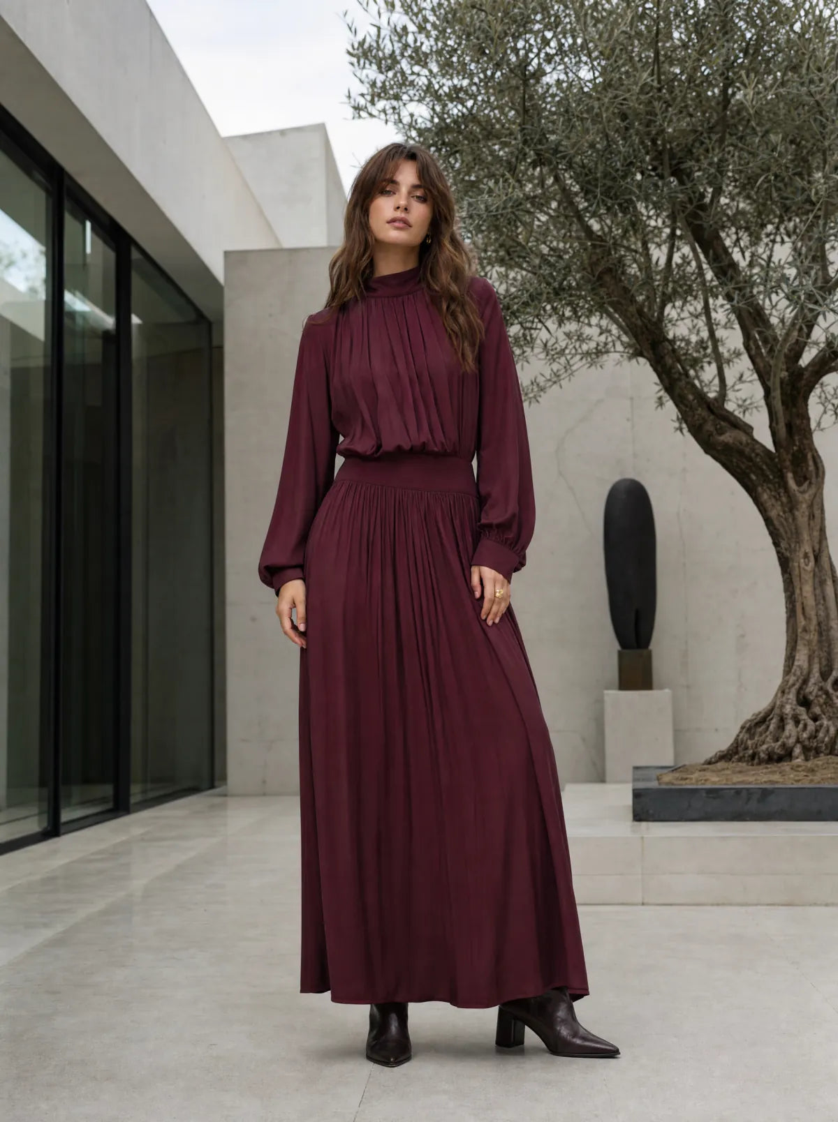 Woman in a burgundy long-sleeve maxi dress in a contemporary courtyard