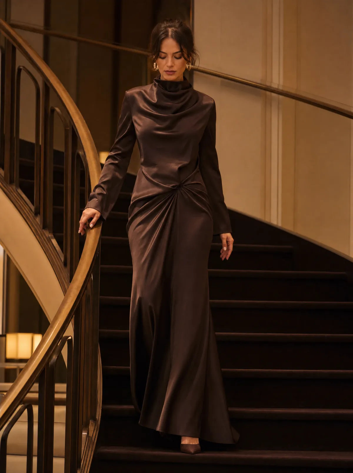 Woman in an espresso satin maxi dress descending a curved hotel staircase