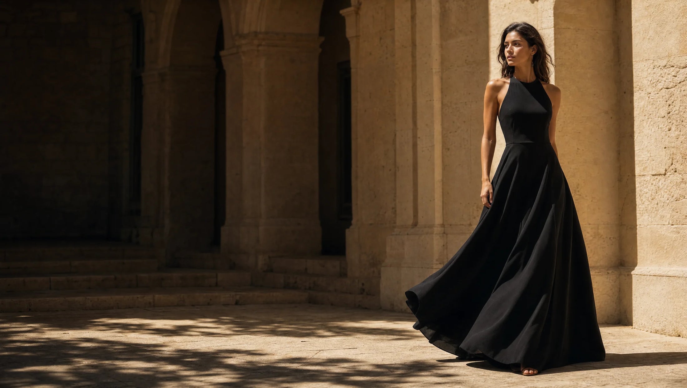 Woman wearing a flowing black maxi dress in a sunlit limestone arcade