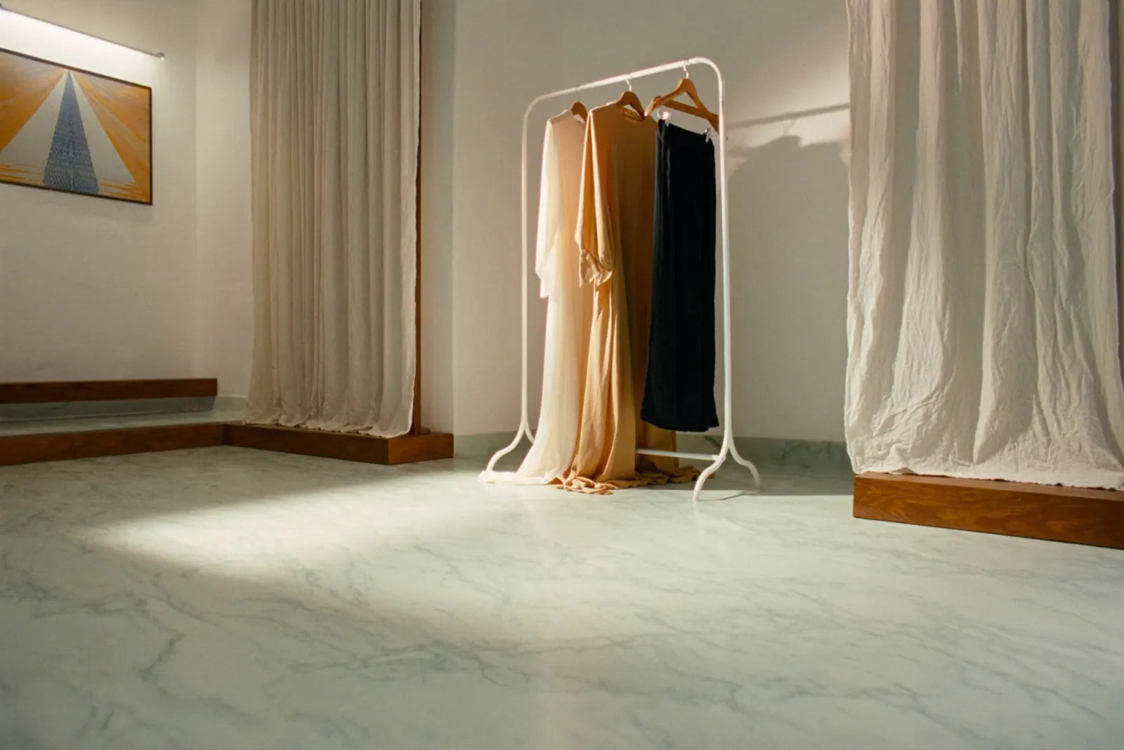 Three neutral maxi dresses on a clothing rail in a sunlit studio