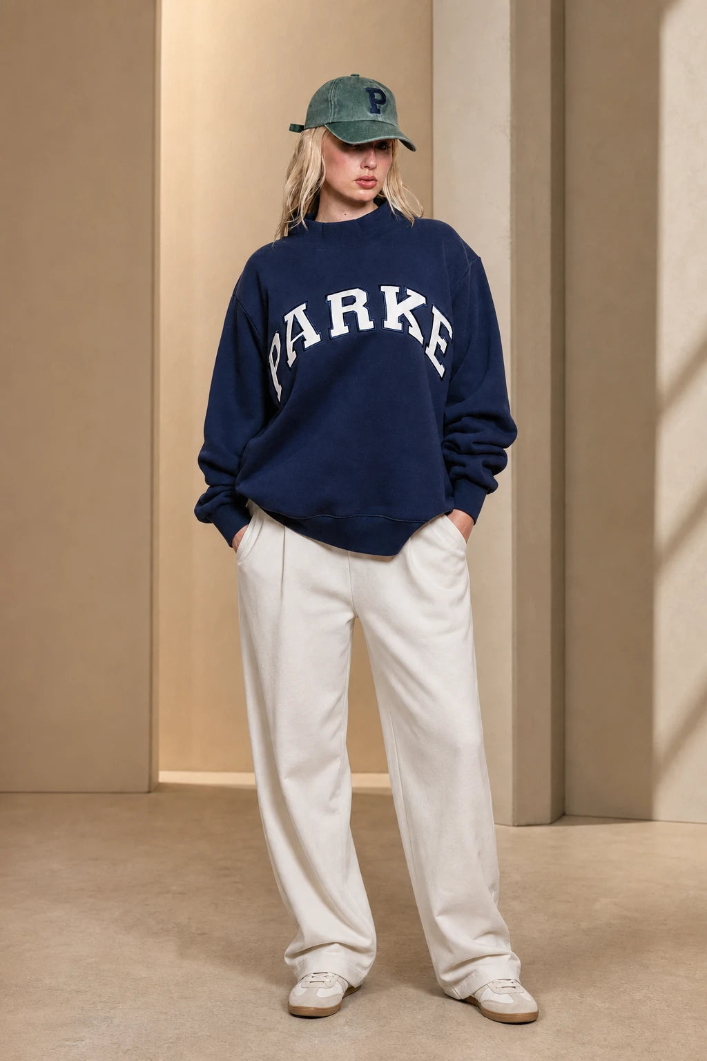 Woman wearing an oversized navy varsity sweatshirt in a warm neutral studio